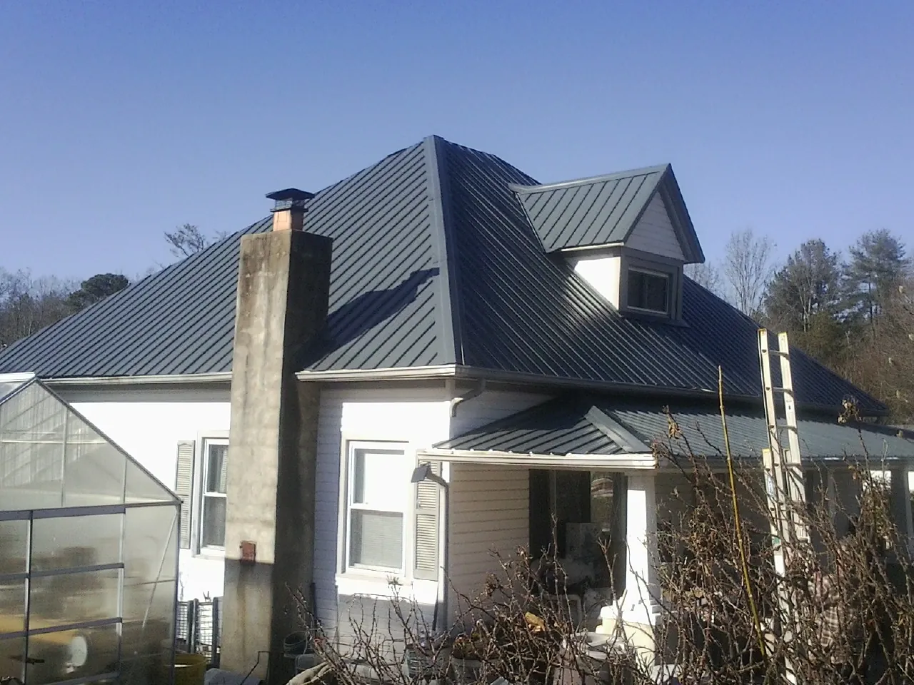 Dark blue standing seam metal roof on a white farmhouse with dormer — Slate & Tile Roof Repair by Roofing Brothers in Menomonie