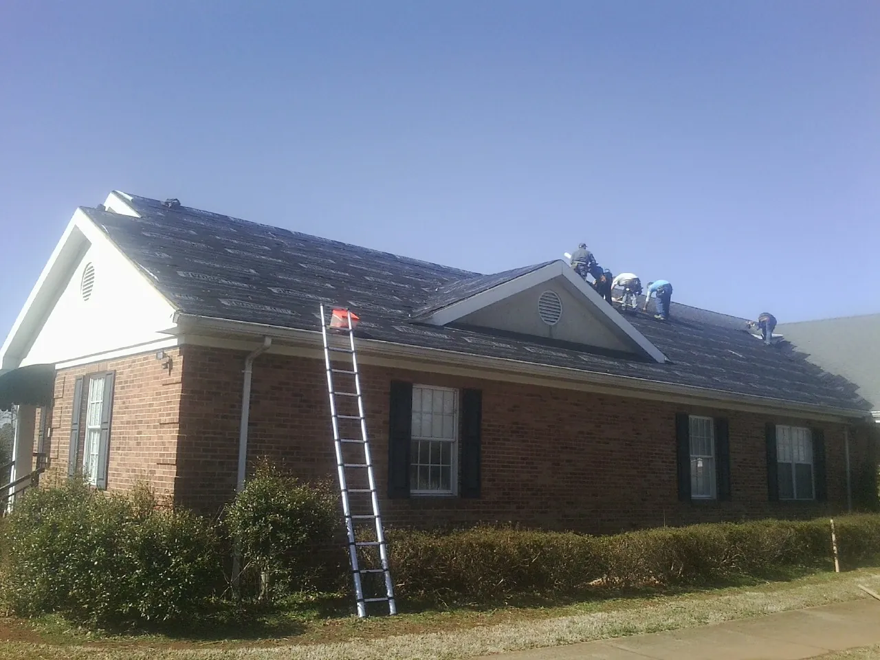 Crew tearing shingles off a brick ranch roof with a ladder set — Metal Roof Repair work by our crew in Menomonie