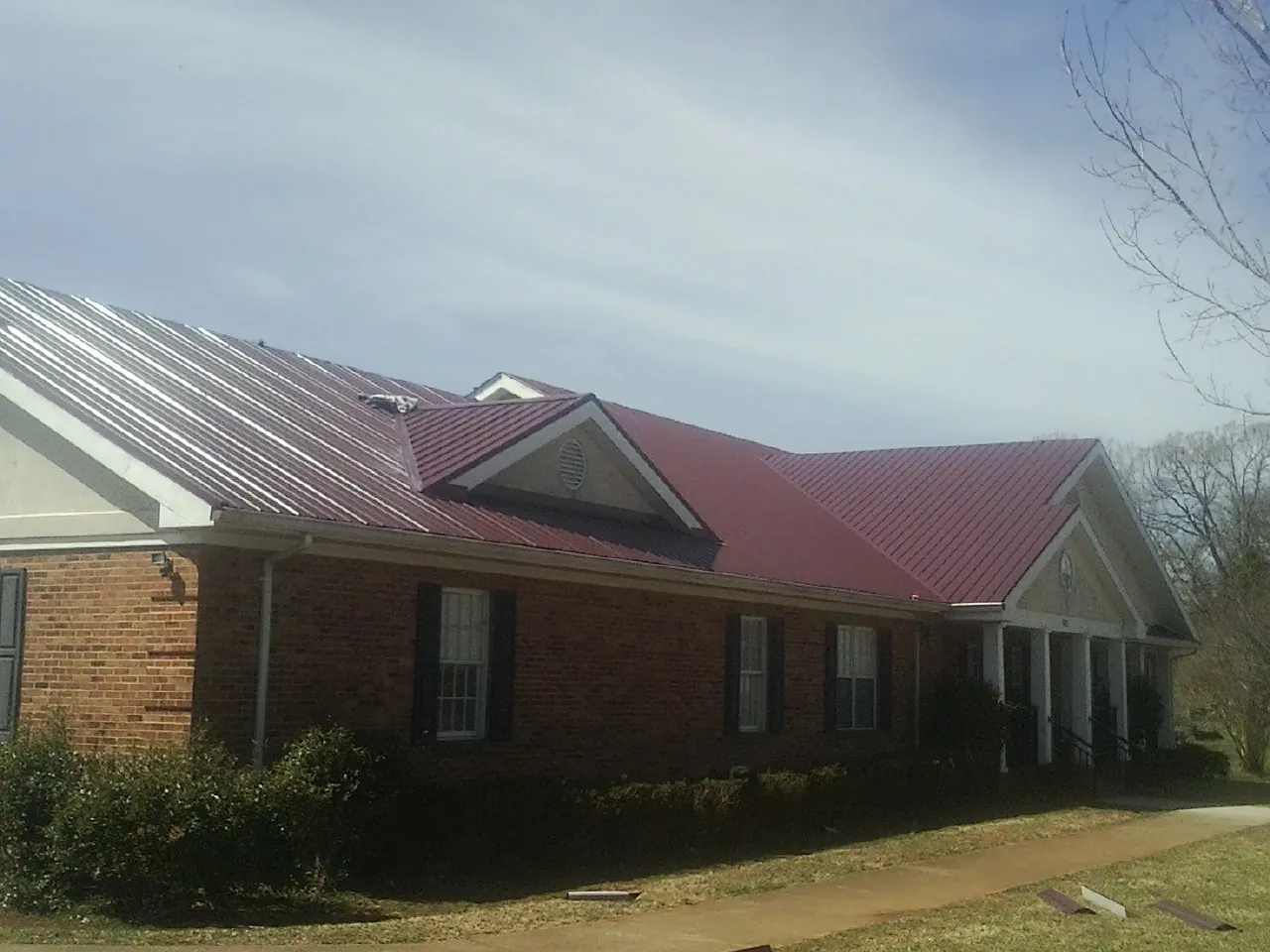 Red metal roof with gabled entries on a long brick building, from a Hail Damage Roof Repair job in Menomonie