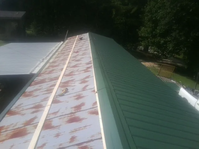 Old rusted panels beside newly installed green metal roofing — Wind Damage Roof Repair by Roofing Brothers in Menomonie