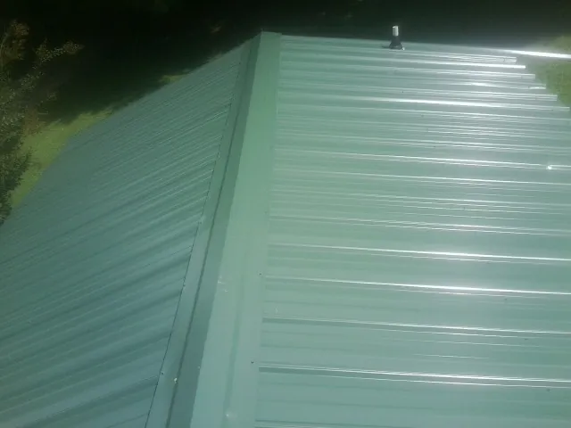 New green metal panels meeting at the ridge of a roof — Flat Roof Repair work by our crew in Menomonie