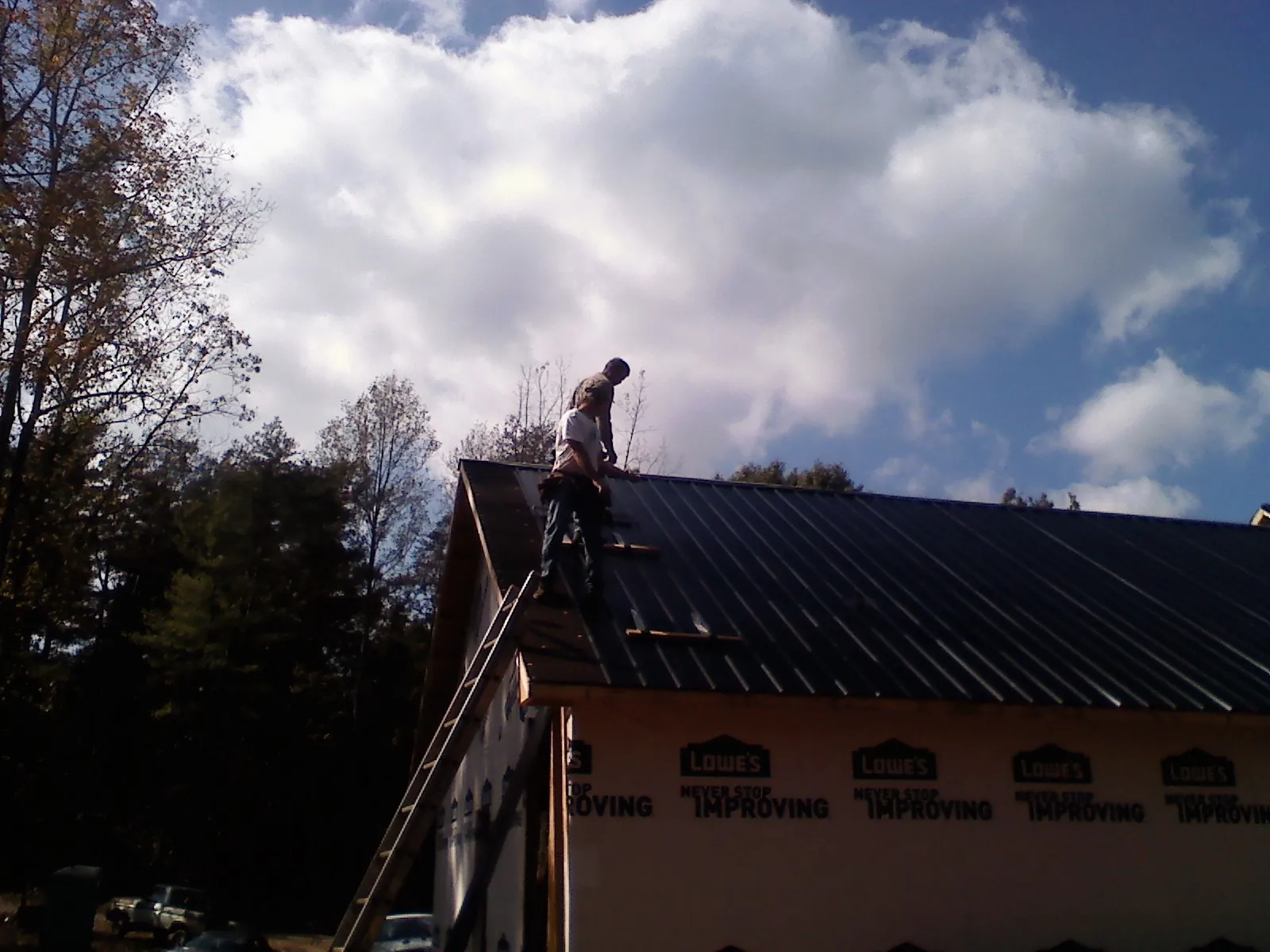 Roofer fastening dark metal panels high against a cloudy sky, from a Roof Inspection job in Menomonie