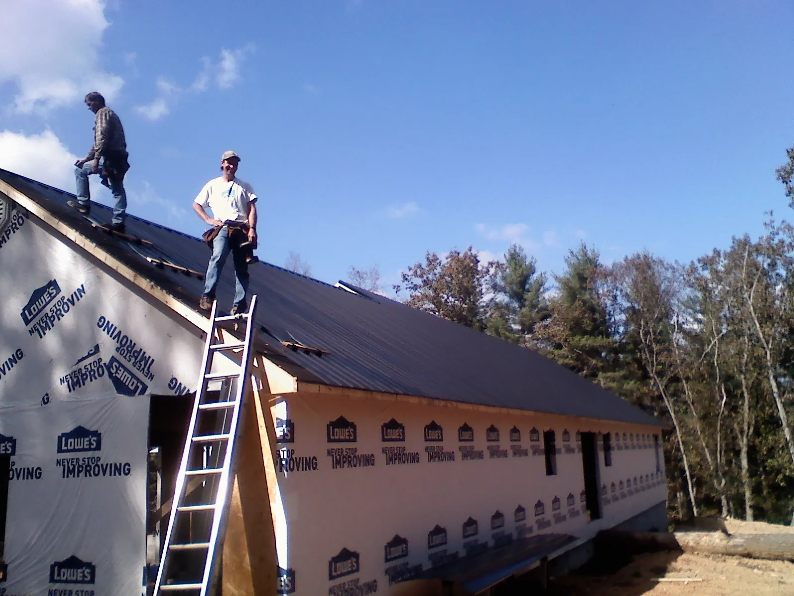Two roofers standing on a long dark metal roof over a wrapped building in Menomonie