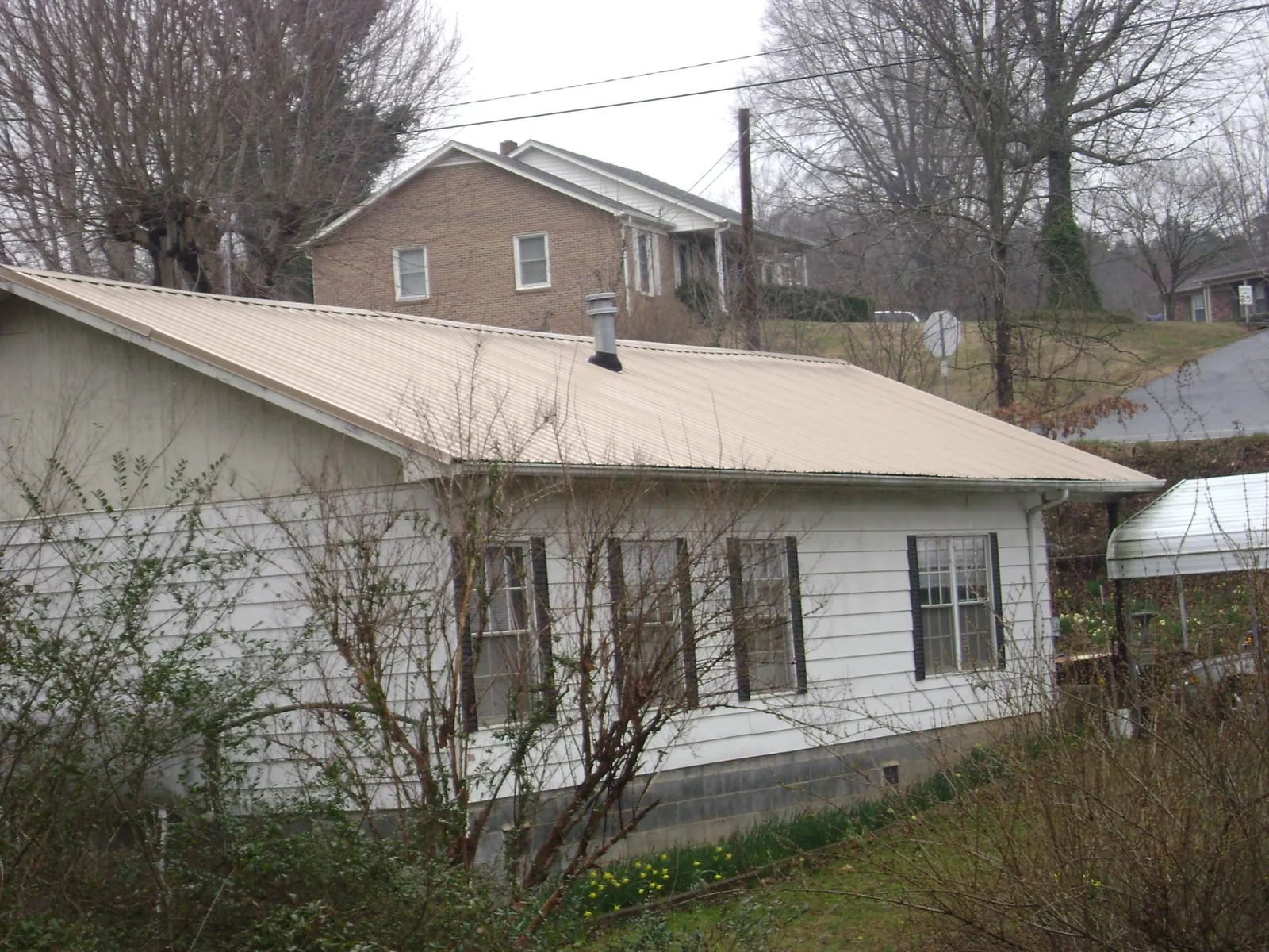 Tan metal roof on a white sided house set into a hillside — Commercial Roofing by Roofing Brothers in Menomonie