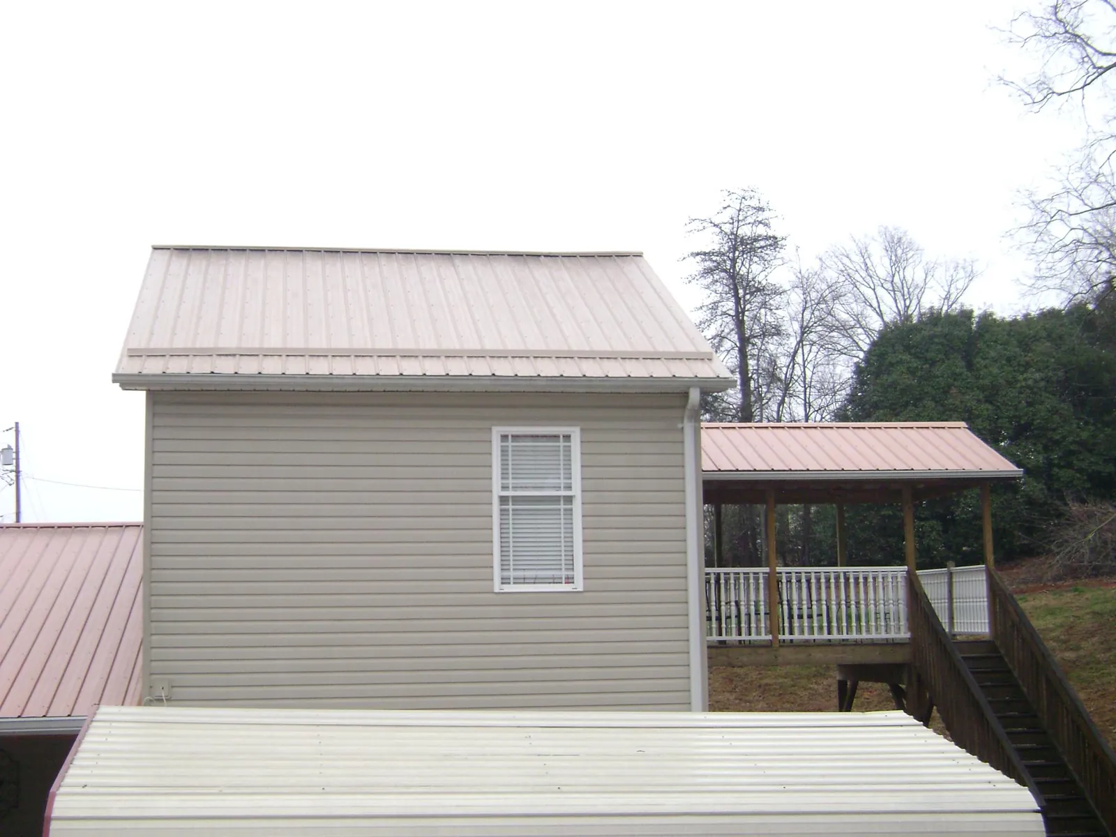 Tan metal roofs on a two story addition and attached porch, from a Roof Replacement job in Menomonie