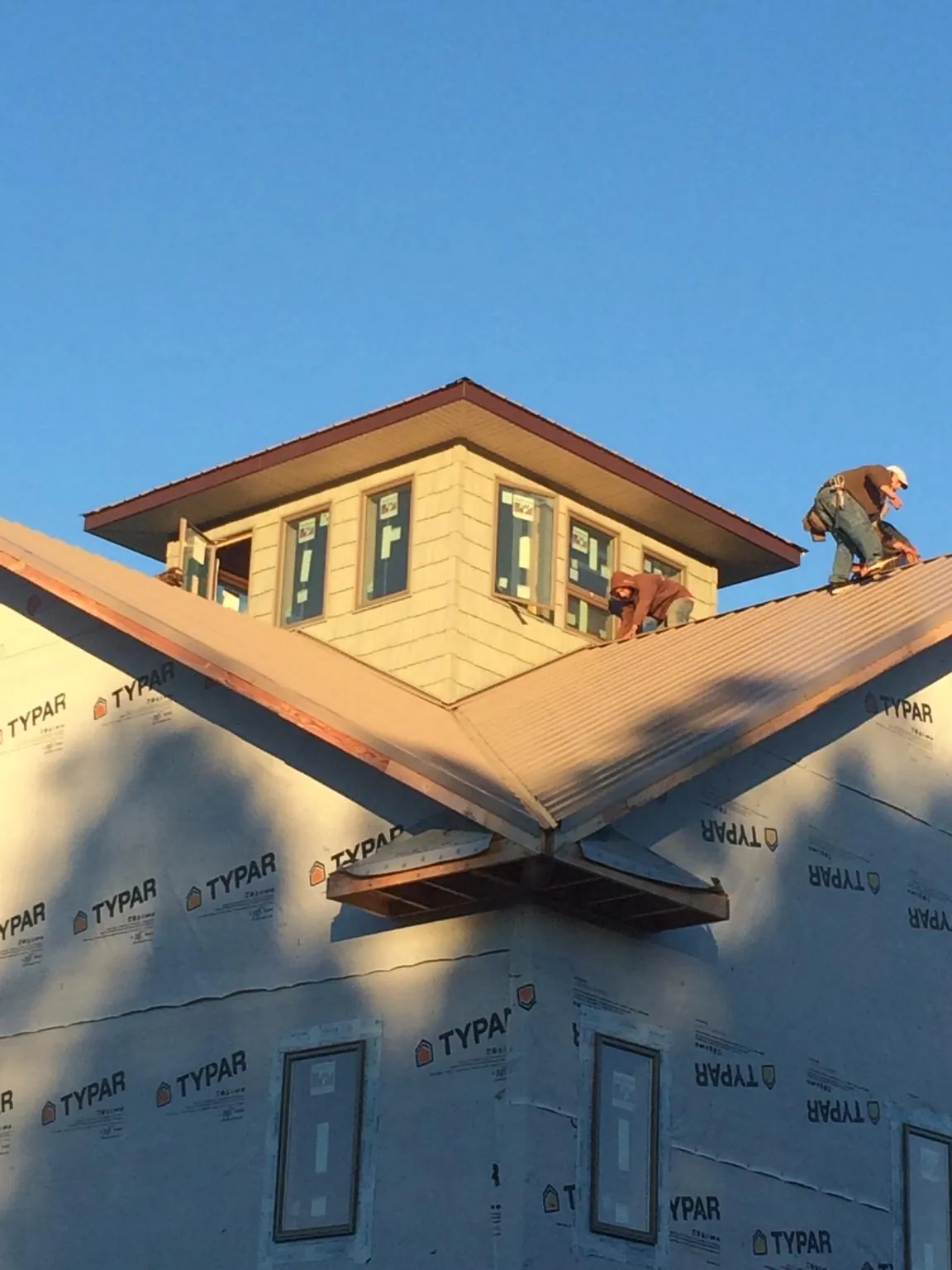 Roofers working around a rooftop cupola on a new metal roof at sunset — Roof Waterproofing in Menomonie by Roofing Brothers